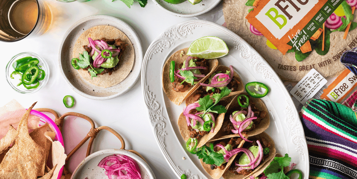 Photo of vegan refried been tacos including pickled onions and vibrant chillis and gluten free sweet potato wraps.